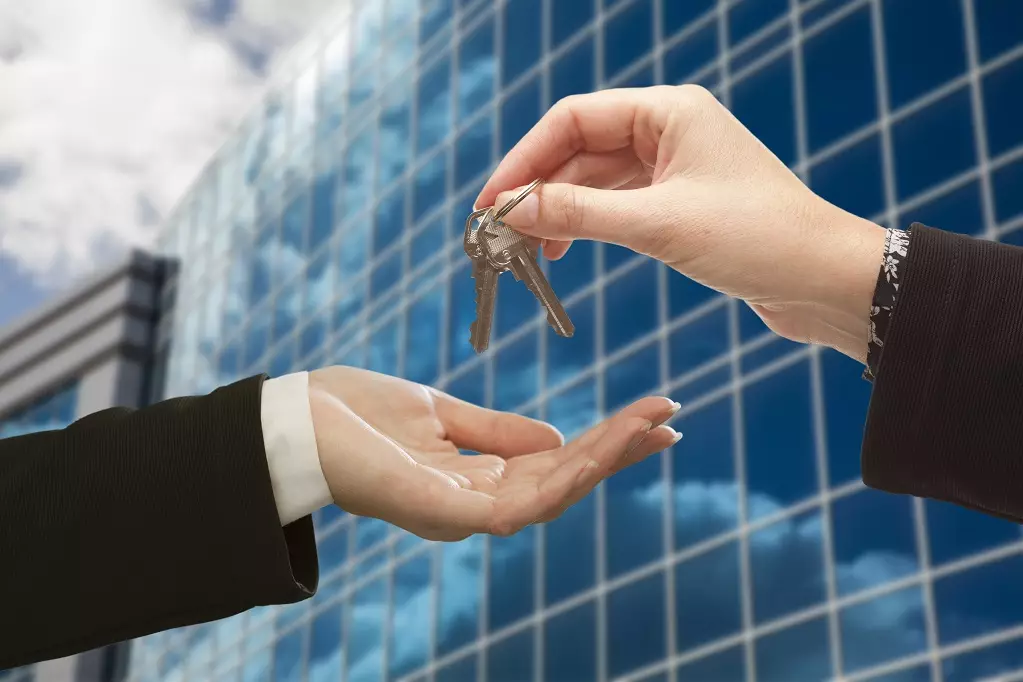 Business Person Handing Over the Keys in Front of Corporate Building